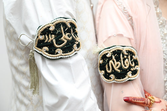 Bride and groom donned in elegant attire, wearing 'Ya Ali' and 'Ya Imam Zamin' symbols, embodying blessings and protection in a Muslim wedding tradition